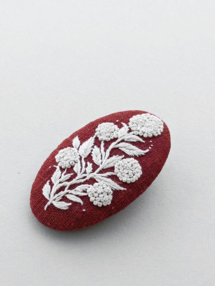 Détail broche rouge en lin avec motif fleur brodé à l'aiguille