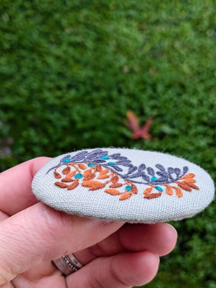 Détail broche en lin brodée à l'aiguille d'une branche de fleurs